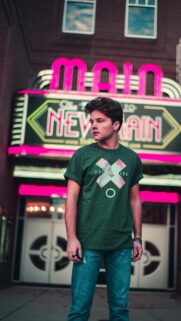 Young Man in Green Shirt Standing Before a Neon Theater Sign Wallpaper