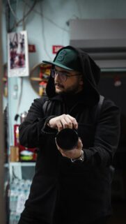 Candid Photographer in Black Hoodie and Green Cap Urban Aesthetic Wallpaper