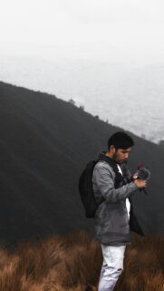 Young Traveler Adjusting Camera Gear on Mountain Peak Phone Wallpaper