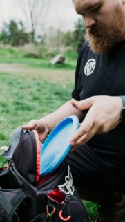 Man Picking Disc Golf Disc from Bag in Nature Mobile Wallpaper
