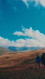 Two Hikers Trekking Through Rolling Golden Mountain Landscape Wallpaper