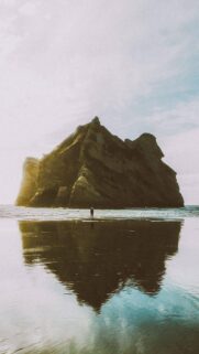 Solitary Figure Standing Before a Majestic Sea Stack at Sunset Mobile Wallpaper