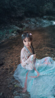 Beautiful Asian Girl in Traditional Hanfu Sitting in a Serene Forest Stream Wallpaper