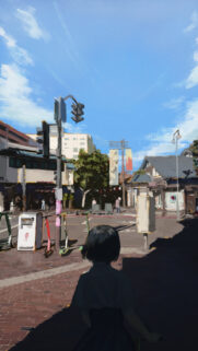 Anime Style City Street Scene with Person Walking in Sunlight High Quality Wallpaper
