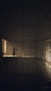 Mysterious Woman Standing in Ancient Dark Library Wallpaper for Mobile