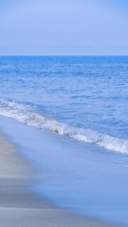 Serene Blue Ocean Waves Rolling onto Sandy Beach Mobile Wallpaper