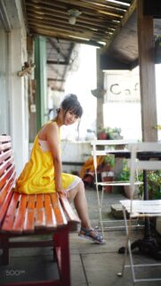 Beautiful Young Woman in Yellow Dress Sitting on Bench at Cafe Wallpaper