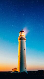 Stunning Lighthouse Under Starry Night Sky Mobile Wallpaper