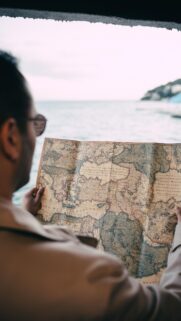 Man Exploring Antique Map of the World overlooking the Sea Phone Wallpaper