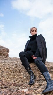 Stylish Woman in Black Fashion Sitting on Rocky Terrain Wallpaper