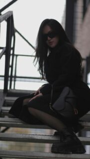 Stylish Woman in Black Coat with Designer Handbag Mobile Wallpaper