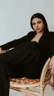 Elegant Woman in Black Blazer Sitting on Rattan Chair Wallpaper