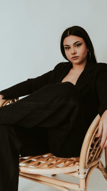 Elegant Woman in Black Blazer Sitting on Rattan Chair Wallpaper