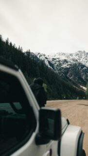 Person Standing by Jeep Overlooking Snowy Mountains Alpine View Wallpaper