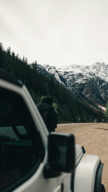 Person Standing by Jeep Overlooking Snowy Mountains Alpine View Wallpaper
