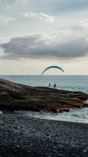 Adventurous Paraglider Over Ocean Waves Mobile Wallpaper