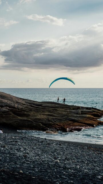 Adventurous Paraglider Over Ocean Waves Mobile Wallpaper