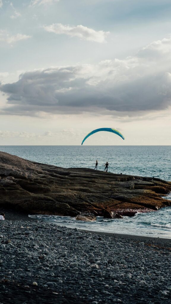 Adventurous Paraglider Over Ocean Waves Mobile Wallpaper