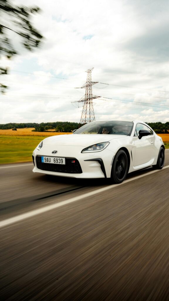White Toyota GR86 Sports Car Speeding on Country Road Wallpaper