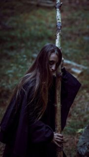 Mysterious Enchantress Holding a Wooden Staff in a Dark Forest Wallpaper