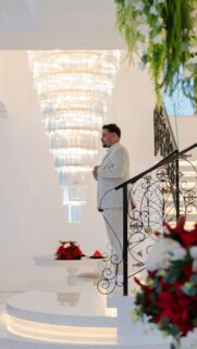 Elegant Man in White Suit Standing by Grand Crystal Chandelier Wallpaper