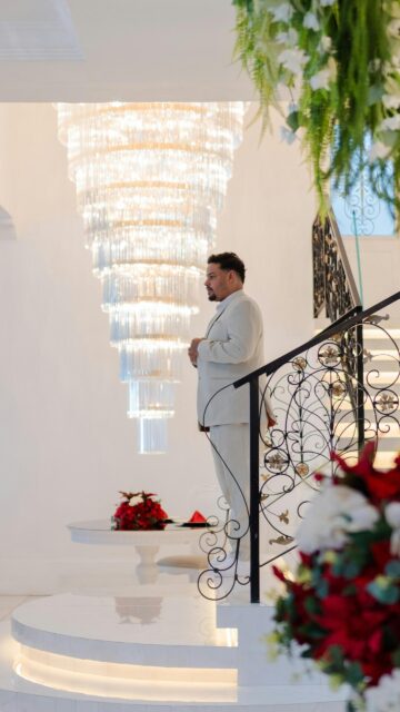 Elegant Man in White Suit Standing by Grand Crystal Chandelier Wallpaper