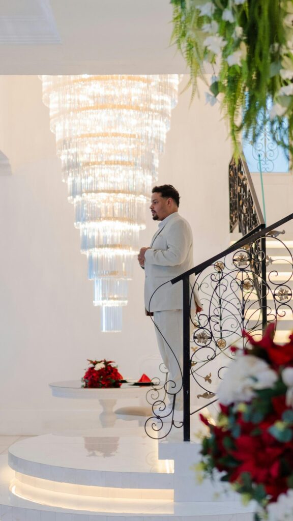 Elegant Man in White Suit Standing by Grand Crystal Chandelier Wallpaper