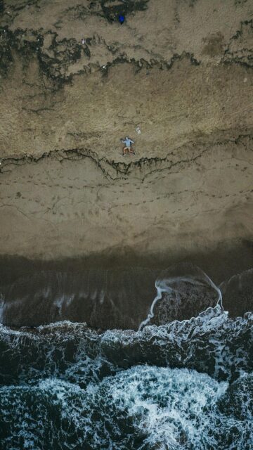 Aerial View of a Person Running on a Sandy Beach Ocean Wallpaper