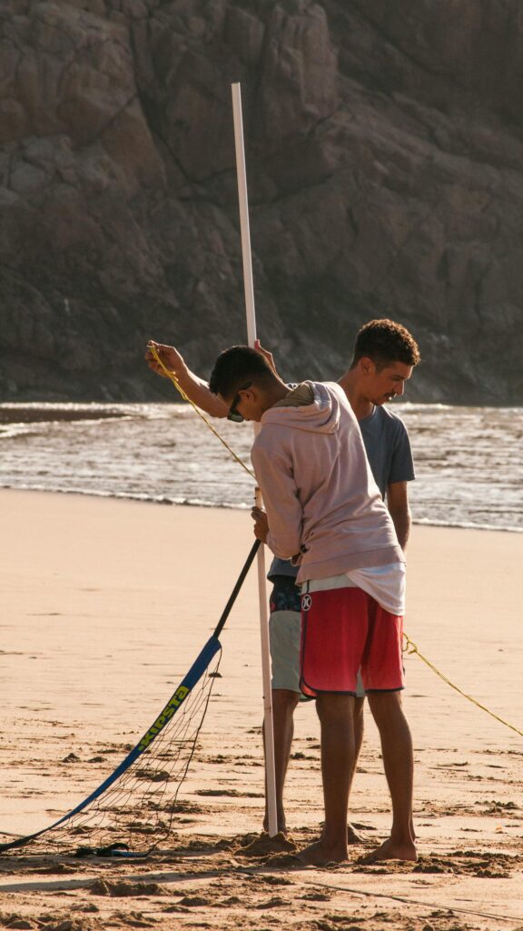 Two Men Setting Up Beach Volleyball Net at Golden Hour Wallpaper