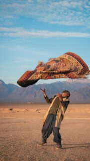 A Man Throwing a Traditional Persian Carpet in the Desert Wallpaper