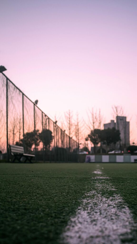 Serene Sunset Sports Field and Bench Mobile Wallpaper
