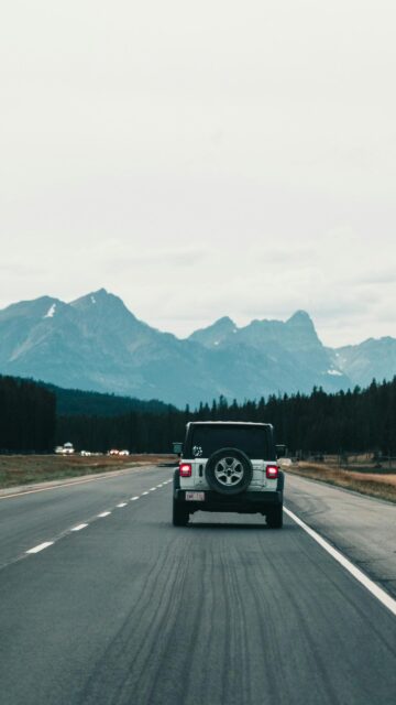 White Jeep Wrangler Driving Towards Majestic Mountains Mobile Wallpaper