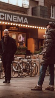 Cinematic Street Scene with Two Men Walking by Theater Lights Wallpaper