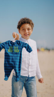 Young Boy Holding Baby Clothes on a Sunny Beach Mobile Wallpaper