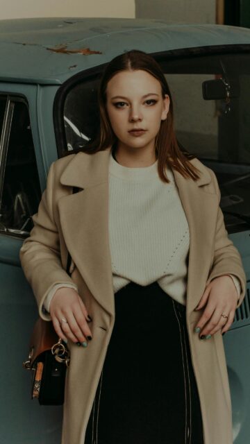 Stylish Girl in Beige Coat Leaning on Vintage Blue Car Wallpaper