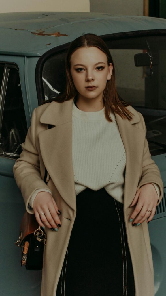 Stylish Girl in Beige Coat Leaning on Vintage Blue Car Wallpaper