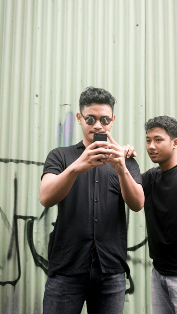 Two Young Men Checking Phone Against Graffiti Metal Wall Wallpaper