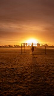 Lone Figure Standing in Soccer Goal at Golden Sunset Mobile Wallpaper