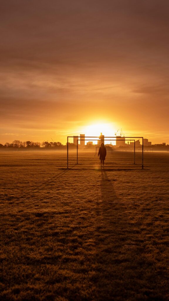 Lone Figure Standing in Soccer Goal at Golden Sunset Mobile Wallpaper