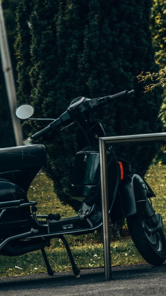 Vintage Black Vespa Scooter Parked in Lush Greenery Wallpaper