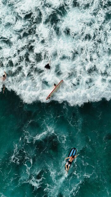Aerial View of Surfers Riding Ocean Waves Mobile Wallpaper
