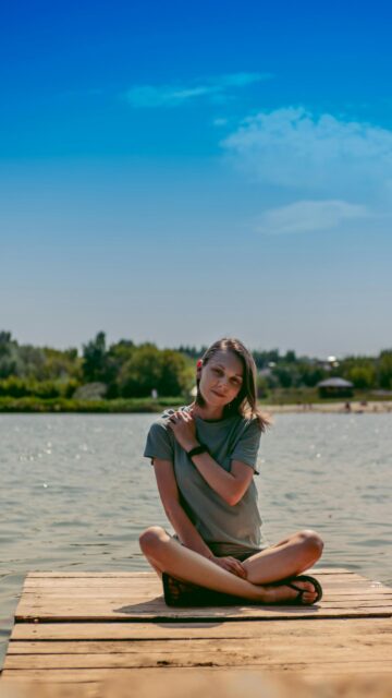 Serene Woman Sitting on Wooden Dock by the Lake Phone Wallpaper
