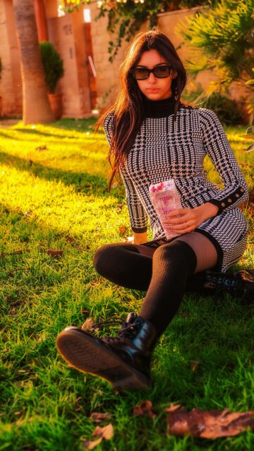 Stylish Woman in Houndstooth Dress Sitting on Grass Mobile Wallpaper