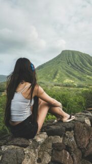 Girl Sitting on Rock Overlooking Lush Green Mountain Landscape Wallpaper