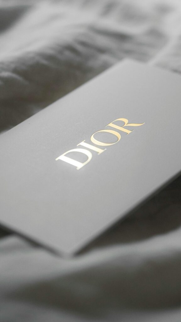Elegant Dior Logo Gold Embossed on Grey Background Phone Wallpaper