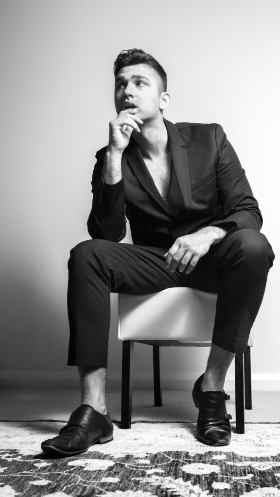 Stylish Man in Black Suit Posing on Chair Mobile Wallpaper