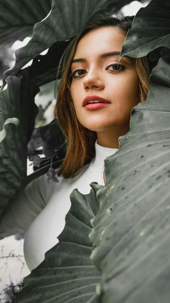 Beautiful Woman Peeking Through Lush Green Tropical Leaves Mobile Wallpaper