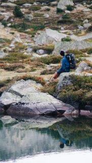 Solo Hiker Resting by a Serene Mountain Lake Mobile Wallpaper