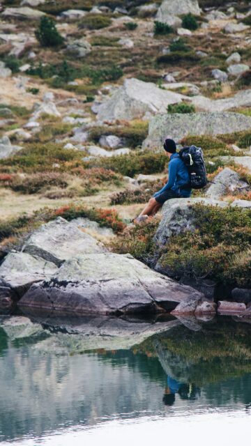 Solo Hiker Resting by a Serene Mountain Lake Mobile Wallpaper