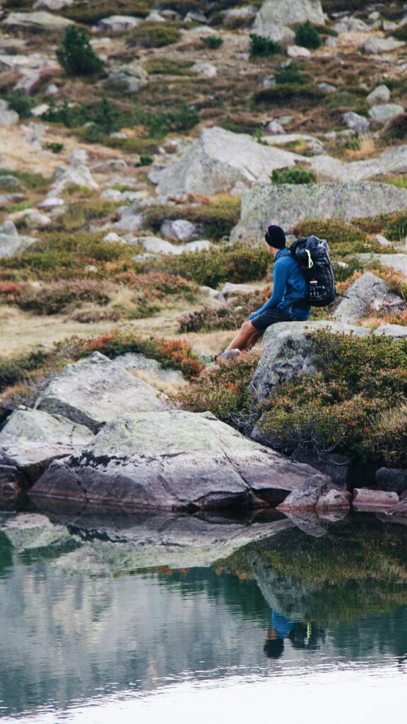 Solo Hiker Resting by a Serene Mountain Lake Mobile Wallpaper